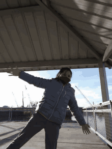 a woman wearing a mask and a blue jacket is standing under a roof with her arms outstretched