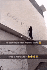a snapchat of a person standing on a wall that says " baise la me " on it
