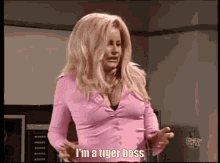 a woman in a pink shirt is standing in a room and says `` i 'm a tiger boss '' .