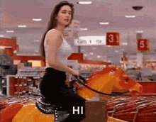 a woman is riding a merry go round in a store and says hi .