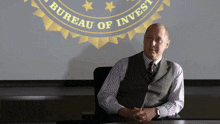 a man sits at a table in front of a screen that says bureau of invest
