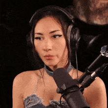 a woman wearing headphones and a blue choker stands in front of a microphone