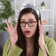 a woman wearing glasses , a headband and a green shirt is making a surprised face .