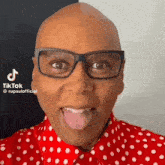 rupaul is wearing glasses and a polka dot shirt and sticking his tongue out .