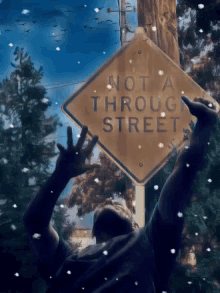 a man is reaching up towards a sign that says " not a through street "