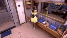a woman in a yellow dress is standing in a bathroom .