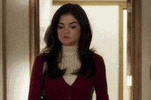 a woman is standing in a hallway wearing a red cardigan and a white turtleneck .