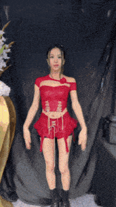 a woman in a red top and shorts stands in front of a black curtain