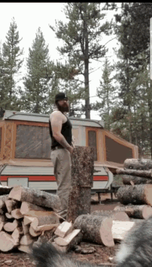 a man is standing next to a pile of logs in front of a trailer