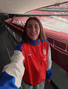 a woman in a red white and blue nike jacket is taking a selfie
