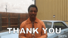 a man stands in front of a blue car and says " thank you "