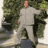 a man in a plaid suit is jumping in the air with a suitcase behind him .