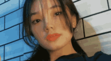 a close up of a woman 's face against a blue brick wall .