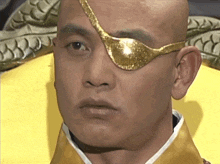 a bald man wearing a gold eye patch and a yellow robe
