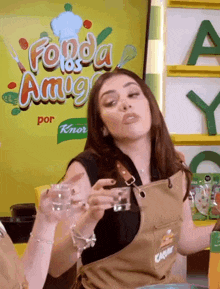a woman in an apron is holding a glass in front of a sign that says fonda amigos
