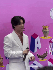 a man in a white suit is holding a microphone in front of a pink wall with the letter a