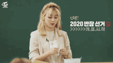 a girl with blonde hair is holding a piece of paper in front of a chalkboard with twice written on it