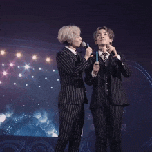 a man in a striped suit holds a microphone while another man holds a light stick