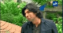 a man with long hair is standing in front of a blue sign that says ' a ' on it