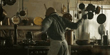 a man in an apron is standing in a kitchen holding a pot