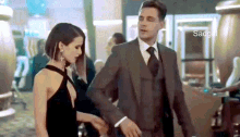 a man in a suit and tie is holding a woman 's hand in a casino .