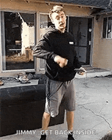 a man in a black hoodie and grey shorts is standing in front of a couch and a window .