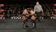 two wrestlers are wrestling in a ring with a referee standing behind them
