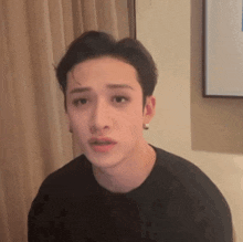 a young man is making a funny face in a room while wearing a black shirt .