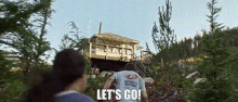 a group of people are walking towards a house in the woods and saying `` let 's go '' .