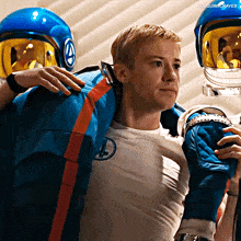 a man wearing a white shirt with a cross on it is being carried by another man wearing a blue helmet
