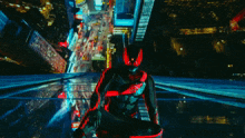 a man in a red and black spiderman suit is standing on a ledge overlooking a city at night