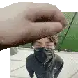 a man wearing a face mask and glasses is being held by a hand .