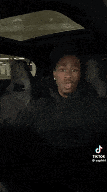 a man is sitting in a car making a funny face and pointing at the camera .