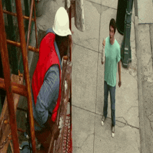a man in a green shirt is standing next to a man in a hard hat
