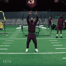 a man in a maroon jacket stands on a soccer field with the word him on the bottom