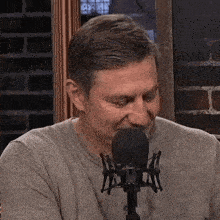 a man is talking into a microphone while wearing a grey shirt