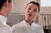 a woman in a white chef 's coat with the letter m on the front