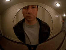 a man in a leather jacket is standing in a hallway looking at the camera