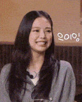 a woman with long black hair is smiling and wearing a gray sweater and headphones .