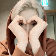 a person wearing a hoodie making a heart shape with their hands