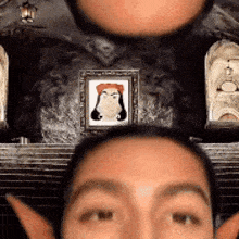 a close up of a person 's face with a picture of a woman on the wall behind them