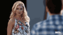 a woman in a floral dress is standing in front of a man in a blue shirt .