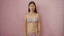 a woman in a bikini is standing against a pink background .