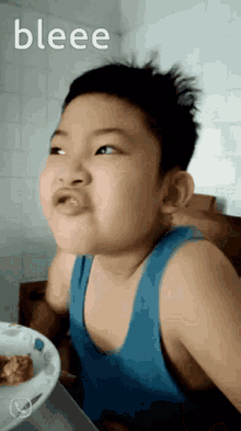 a young boy in a blue tank top is sitting at a table with a plate of food and the word bleee on the bottom