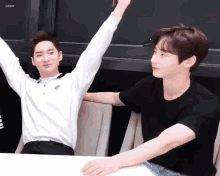 two men are sitting at a table with their arms in the air