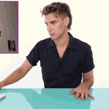 a man in a black shirt sits at a table with his hands on the table