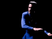 a man in a blue shirt and blue shorts is dancing in a dark room .