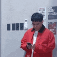 a man in a red jacket is looking at his cell phone in a room .