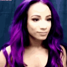a woman with purple hair is wearing a black tank top and looking at the camera .