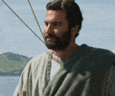 a man with a beard and a green robe stands in front of a body of water